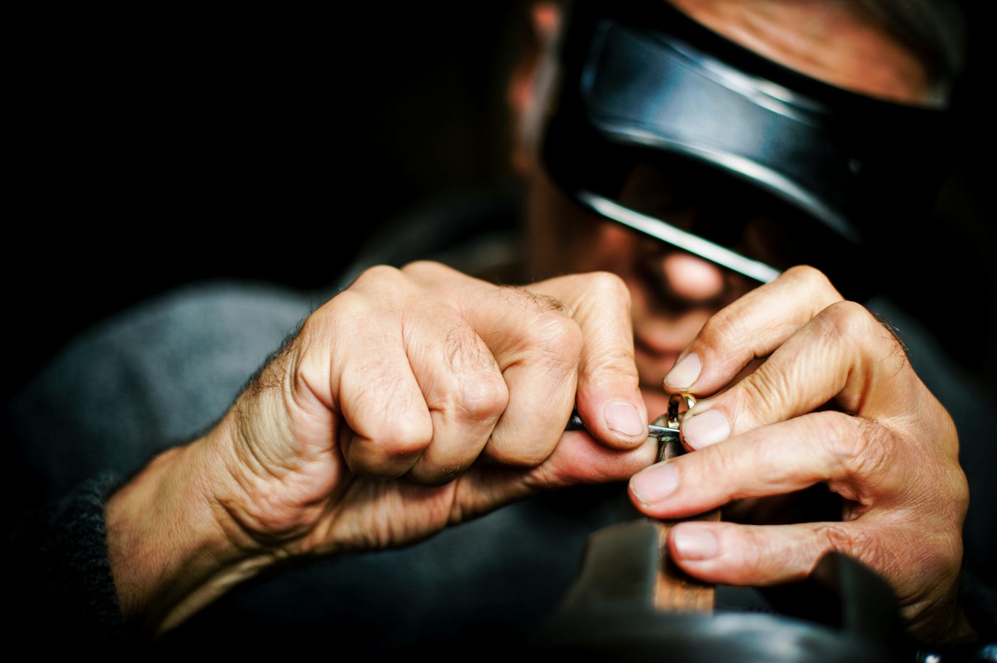 A jeweler working on a gold ring at the bench under a magnifying loupe